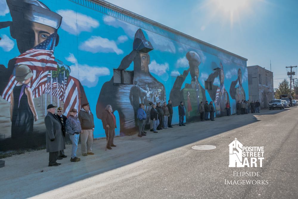 A mural dedication was held on the morning of Veterans Day, 2017 where this above image was taken. It depicts veterans in attendance representing their branch by standing in front of the respective figure